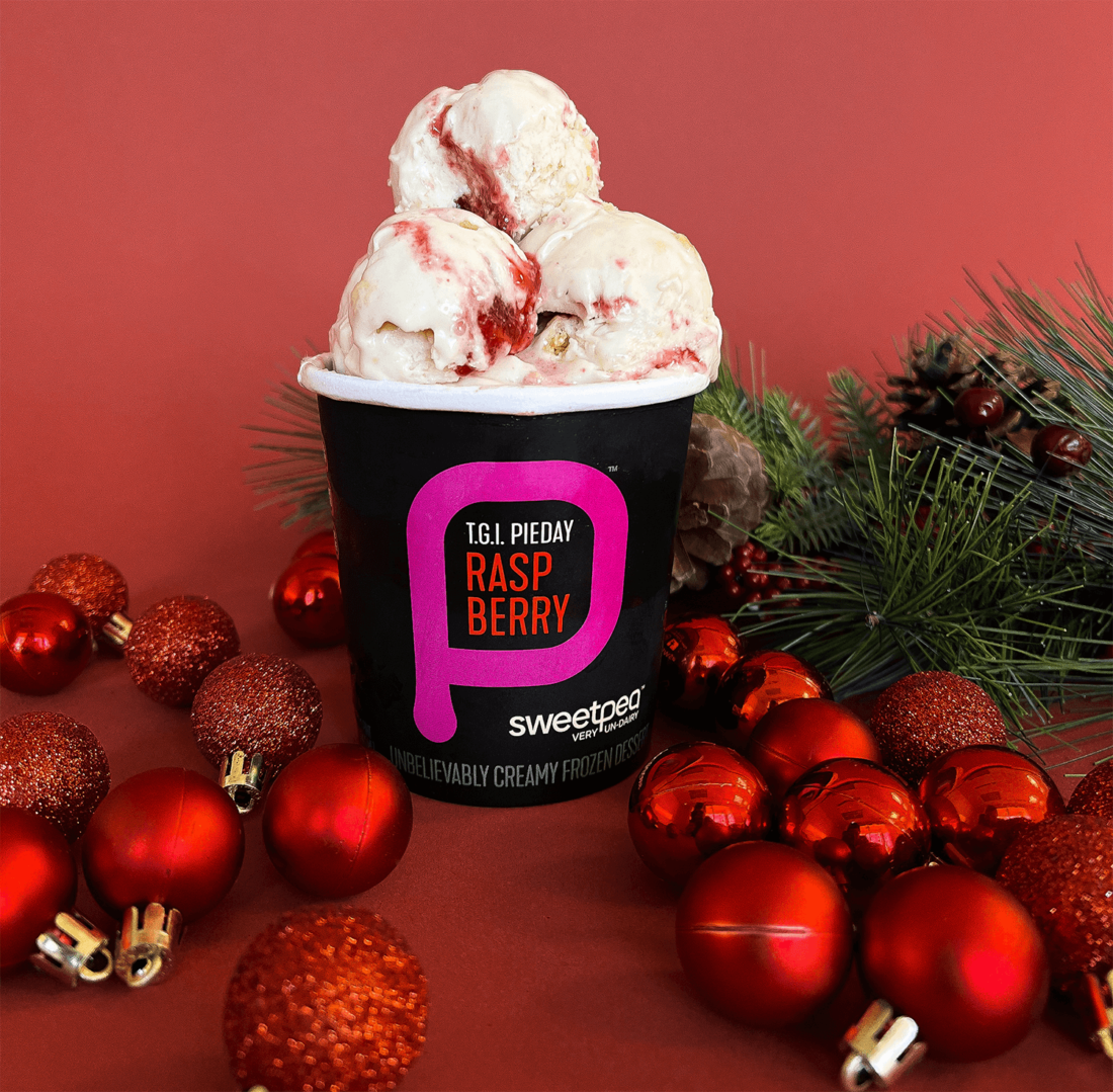 Pint of SweetPea Raspberry plant-based ice cream in front of red background with red Christmas ornaments