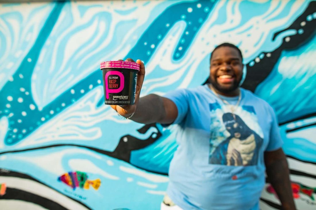 Man holding pint of raspberry sweetpea non-dairy ice cream in front of ocean mural.