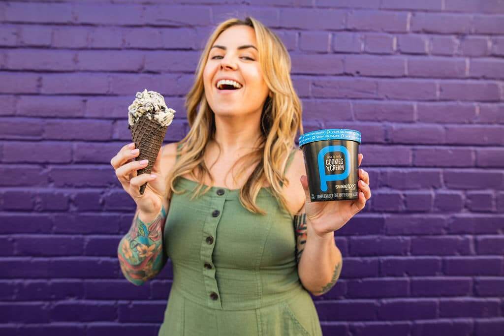 Woman standing with SweetPea non-dairy ice cream pint and cone.