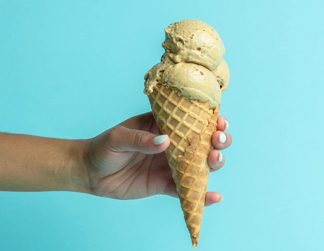 SweetPea Must Do Cold Brew plant-based ice cream in a waffle cone held in front of teal background.